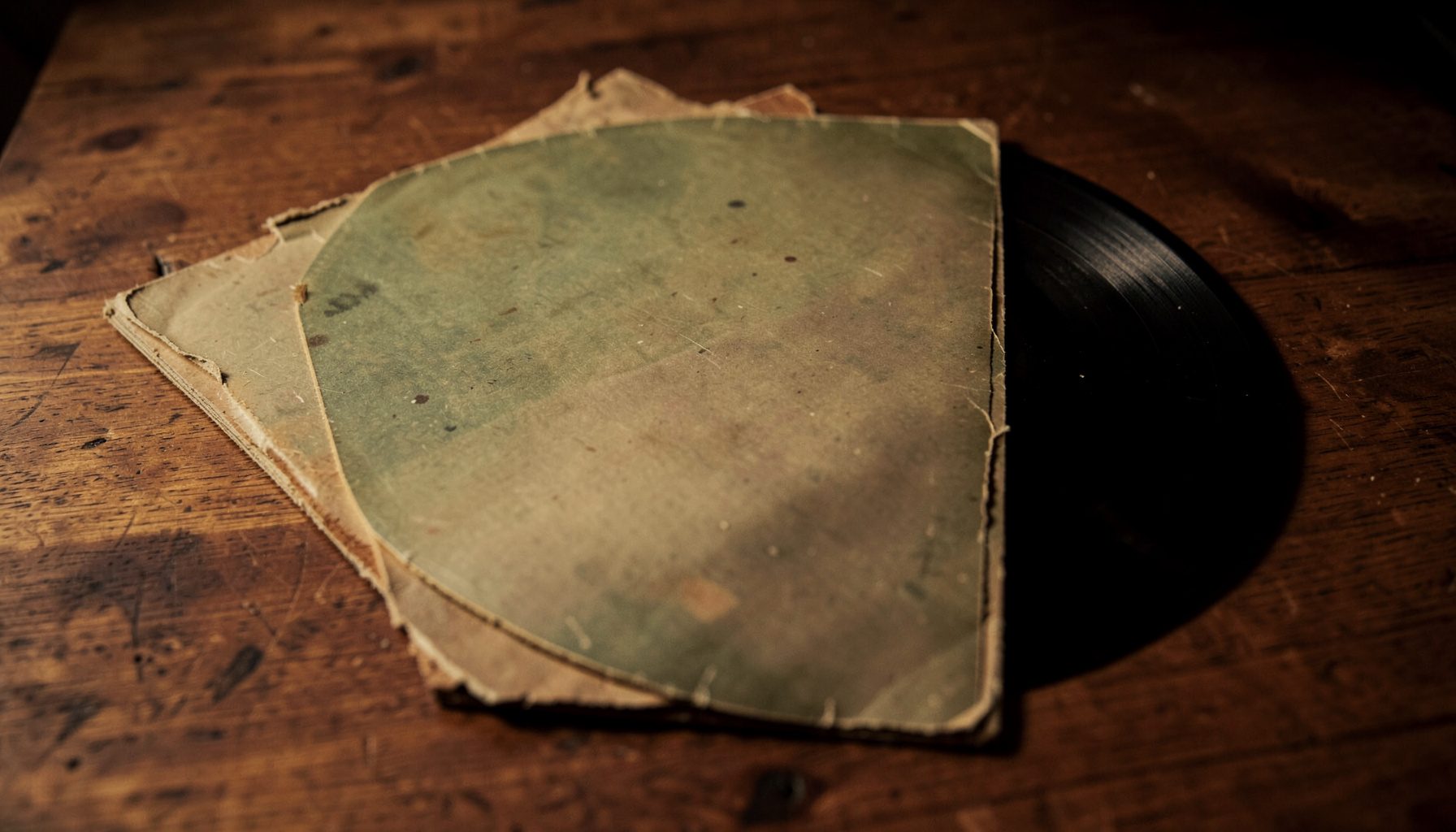 Vintage vinyl record sleeve with muted earth tones and worn edges, resting on a wooden surface under dim warm light